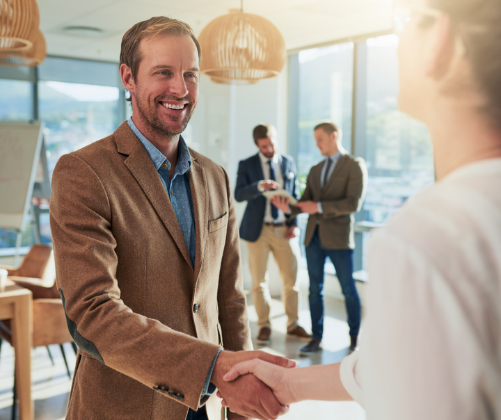A smiling professional shaking hands with a colleague in a modern office, representing the decision of buying a business instead of starting one from scratch.