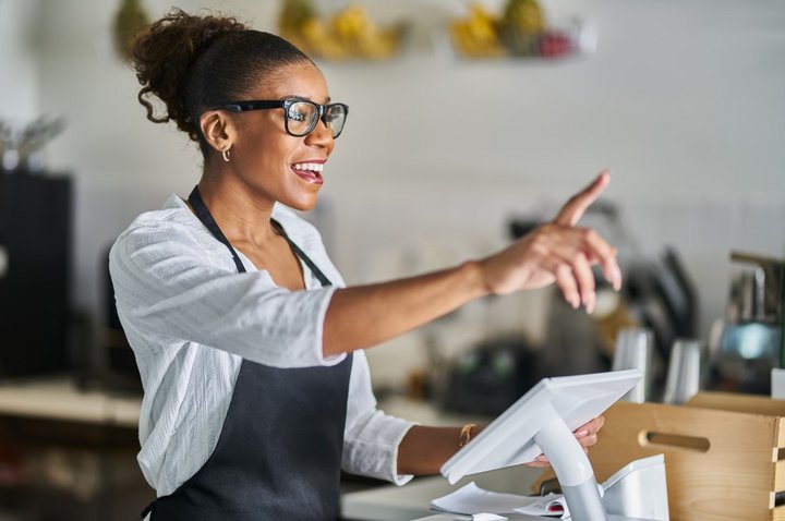 friendly shop assistant waving and greeting customers in store while at POS terminal counter