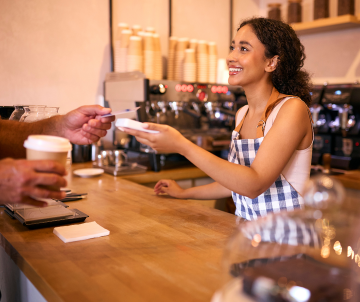 Young small business owner accepting a credit card payment at a coffee shop counter representing small business survival and failure statistics